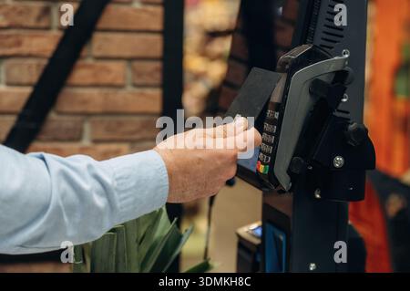 Seitliche Nahaufnahme eines Mannes, der im Lebensmittelgeschäft mit Kreditkarte bezahlt. Stockfoto