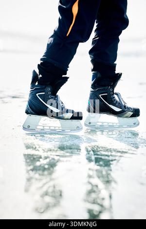 Eislaufsport auf dem gefrorenen See mit Rissen und Schnee im Winter. Nahaufnahme des Eiskunstläuferbeins Stockfoto