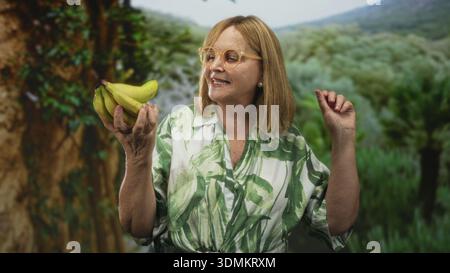 Die Frau hält einen Haufen grüner Bananen in der Hand und lächelt, während sie die Früchte in einem sonnendurchfluteten Wald ansieht; Neugier auf Zufriedenheit. Stockfoto