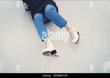 Die Beine und Schlittschuhe eines gefallenen Mädchens auf dem Eis, die einen Moment des Ausrutschens oder Sturzes während des Schlittschuhens zeigen. Stockfoto