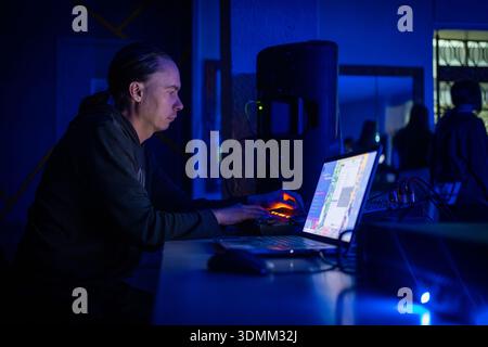 Ein Mann arbeitet als Tontechniker oder DJ in einer dunklen Umgebung und verwendet einen Laptop und eine Mischkonsole, um die Audiopegel für ein Konzert, einen Club oder eine Disco einzustellen. Stockfoto