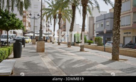 Sonnendurchflutete mediterrane Straßenszene mit Palmen, Bürgersteigen und Gebäuden in einer weichen, verschwommenen Bokeh-Straße; Hintergrund im Hintergrund mit ruhiger Umgebung. Stockfoto