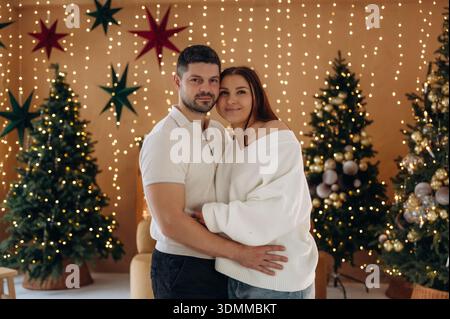 Pärchen stehen im weihnachtlich dekorierten Zimmer, Vorstellung von Feiertagen und Familie. Stockfoto