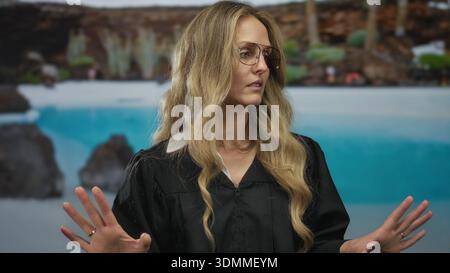Frau hebt Hand im Resort, während der junge blonde Richter in Uniform draußen neben dem Poolhotel steht. Stockfoto