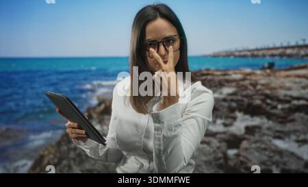Frau, die Tablette hält und mit dem Finger auf die Tablette zeigt, Brille und weißes Hemd im Studio trägt; Konzentration. Stockfoto