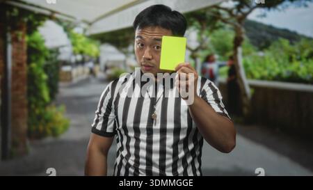 Der Schiedsrichter trägt ein gestreiftes Trikot, hält die gelbe Karte und zeigt mit dem Finger auf die Straße. Stockfoto
