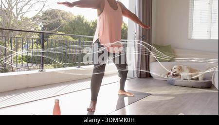 Ausgleichende Frau in rosa Top schwarzen Leggings, die Yoga auf der Matte am Balkon mit rosa Flasche macht Stockfoto