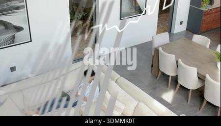 Arbeitender Mann, der auf einem Laptop auf einem cremefarbenen Sofa in einem offenen Wohn-Essbereich mit Jalousien tippt Stockfoto