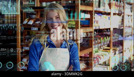 Lächelnder Besitzer mit blauem Denim-Hemd und leichter Schürze im Geschäft mit Holzregalen und Diagrammen Stockfoto