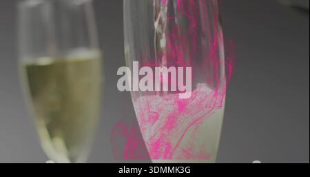 Champagnerflöte mit blassem Bläschen auf dunklem Balken, mit links verschwommener Flöte, magentafarbenem Glanz Stockfoto