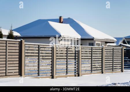 Wohnhaus hinter langem horizontalen Holzzaun, saubere Architektur und schneebedeckter Hof, Haussicherheitskonzept mit privatem Außenbereich und Gehweg Stockfoto