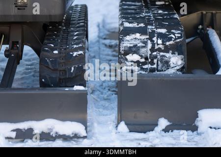 Winterbauarbeiten mit zwei Baggern, kontrastierenden Ketten und Absperrplatten in Nahaufnahme, Schnee und Eis zwischen den Maschinen Stockfoto