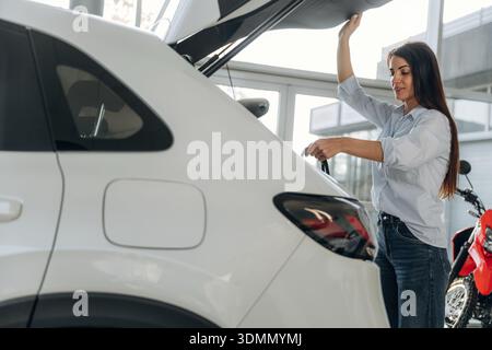 Blick von der Seite. Seitenansicht einer Frau, die nach dem Einkaufen ist und Taschen in den Kofferraum eines Autos steckt. Stockfoto