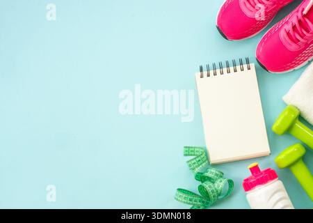 Fitness Flat Lay Hintergrund. Kurzhanteln, Turnschuhe, Maßband, Wasserflasche und Notizblock auf blau. Gesundes Lifestyle-Konzept Stockfoto