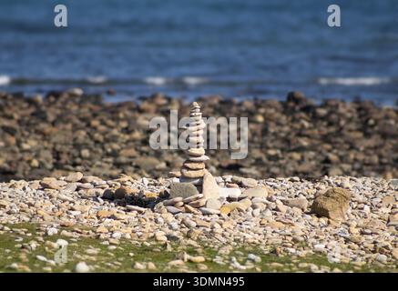 Ein ausgeglichener Steinkairn, der an einem felsigen Küstenstrand steht. Stockfoto