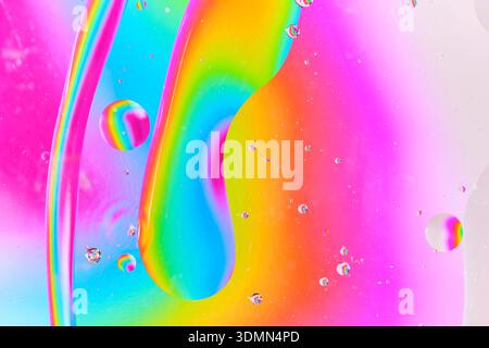 Dynamische Abstraktion mit einem großen langgezogenen Öltropfen, der einer Linse auf einem hellen Spektrumhintergrund ähnelt. Lichtverzerrung durch Wasser Stockfoto