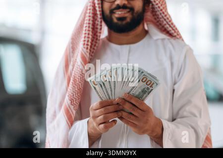 Ein arabischer Geschäftsmann hält Bargeld in einem modernen Autohaus. Stockfoto