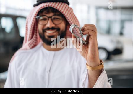 Ein arabischer Geschäftsmann hält Bargeld in einem modernen Autohaus. Stockfoto