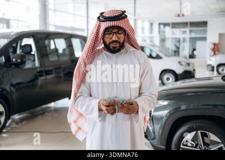 Ein arabischer Geschäftsmann hält Bargeld in einem modernen Autohaus. Stockfoto