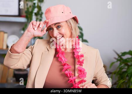 Freundliche Geschäftsfrau In Beige Blazer Mit Rosafarbenem Hut Und Lei Bei Der Bürofeier Stockfoto