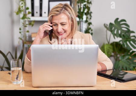Geschäftsfrau Am Telefon, Während Sie An Einem Laptop In Moderner Büroumgebung Arbeitet Stockfoto