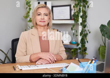 Professionelle Frau Am Schreibtisch Im Modernen Büro, Geschäftsporträt Erfahrener Führungskräfte, Ruhig Und Selbstbewusst Stockfoto