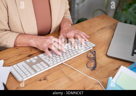 Ältere Frau, die auf der Tastatur am Schreibtisch mit Laptop und Brille für die professionelle Arbeit schreibt Stockfoto