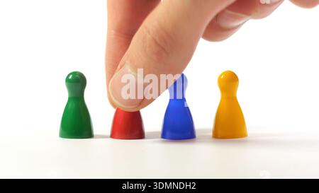 Hand nimmt rote Brettspielspielfigur aus einer Reihe von vier bunten Plastikspielfiguren auf weißem Hintergrund auf, Nahaufnahme Auswahlkonzept für Einstellung, Rekrutierung, Stockfoto