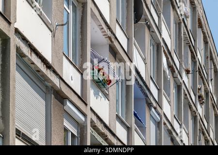Generische, alte, graue Betonfassade aus der kommunistischen Ära, Balkondetails. Ein Balkon mit roten Blumen und gestreifter Markise, Individualität Stockfoto
