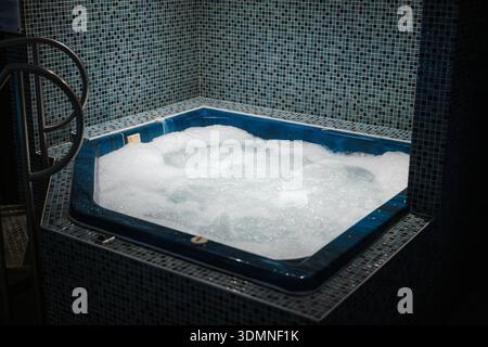 Wannen-Whirlpool im Innenbereich mit sprudelndem Wasser in blau gefliestem Zimmer Stockfoto
