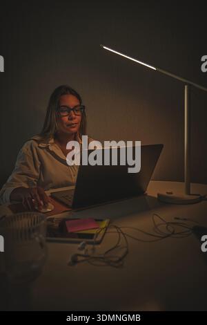 Frau, die von zu Hause aus arbeitet und einen Laptop am dunklen Schreibtisch benutzt Stockfoto
