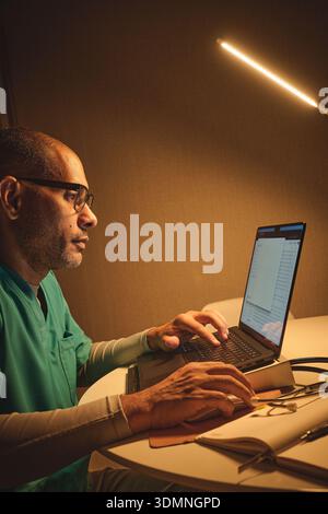 Männlicher Arzt oder medizinischer Fachmann, der am Laptop am Schreibtisch in der Klinik oder im Büro arbeitet Stockfoto