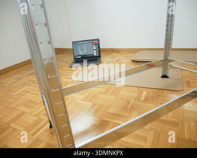Ein Metallregal wird in einem Raum montiert, auf dem ein Laptop mit Montageanweisungen auf einem Holzboden und Pappstücke verstreut sind Stockfoto
