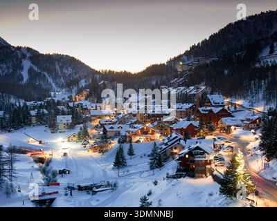 Die schneebedeckten Dächer und funkelnden Lichter aus der Vogelperspektive sorgen für ein warmes Leuchten am dunklen Berghang Claviere, Piemont, Italien. Stockfoto