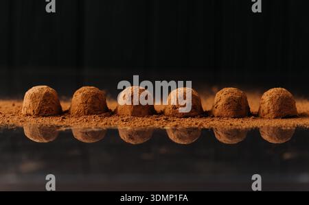 Kakaostaub Schokoladentrüffel hintereinander mit Reflexion auf schwarzem Hintergrund Stockfoto