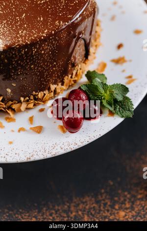 Schokolade glasierter Kuchen mit Kirschen und Minze auf weißem Teller, Nahaufnahme Stockfoto