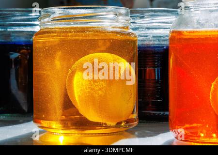 Nahaufnahme eines ostereiers in einer gelben und orangen Lebensmittelfarbstofflösung in einem Glasgefäß auf einem sonnendurchfluteten Küchentisch Stockfoto