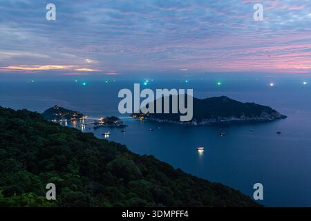 Koh Nang Yuan Insel in der Abenddämmerung mit ruhigem Meer. Blick von Koh Tao, Thailand. Abendhimmel mit schwachen Wolken. Lichter auf kleinen Booten und Insel. Stockfoto