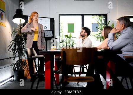 Geschäftsfrau präsentiert Teammitgliedern in einer modernen Büroumgebung während eines Meetings am Vormittag Ideen Stockfoto