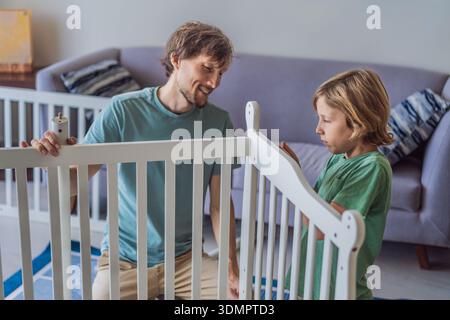 Vater und älterer Bruder bauen zu Hause ein Babybett zusammen und bereiten sich auf die Ankunft eines Neugeborenen vor. Herzlicher Familienmoment voller Sorgfalt und Vorfreude. Elternschaft Stockfoto