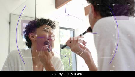 Make-up-Mann in weißem Bademantel, der den Pinsel am Kosmetikspiegel des Badezimmers hält, mit HUD-Überzug Stockfoto