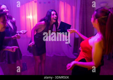 Eine Gruppe glücklicher junger Frauen, die auf einer lebhaften Party tanzen und lachen, umgeben von einer lebhaften und farbenfrohen Atmosphäre, in stilvollen Kleidern Stockfoto