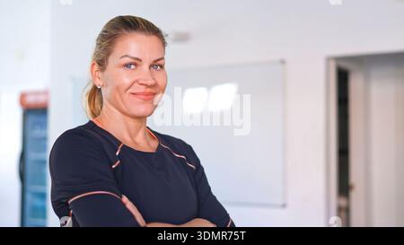 Frau lächelt mit gekreuzten Armen in Sportswear und blickt in die Kamera Stockfoto