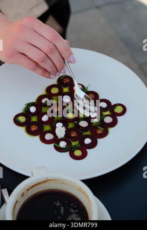 Kunstvoll überzogene Gourmet-Vorspeise mit Roter Bete in geometrischem Muster auf einem weißen Teller mit kleinen Cremepunkten, grünem Öl und frischem Dill Stockfoto