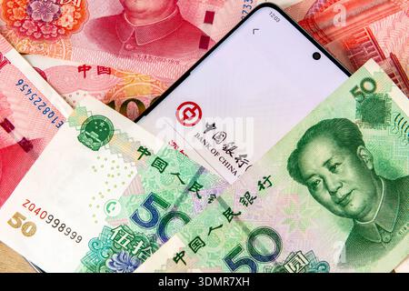 London. UK – Februar 04. 2026. Nahaufnahme des Namens und des Logos der Bank of China auf einer Mobiltelefonanwendung zwischen einem Stapel chinesischer Yuan-Banknoten Stockfoto