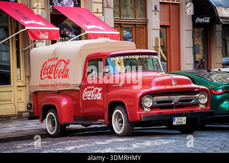 PRAG, TSCHECHISCHE REPUBLIK. März 2025. Ein roter Ford F-100 Pickup-Truck mit Coca-Cola-Logo und einem Canvas-Vordach, geparkt auf einem Kopfsteinpflaster Stockfoto