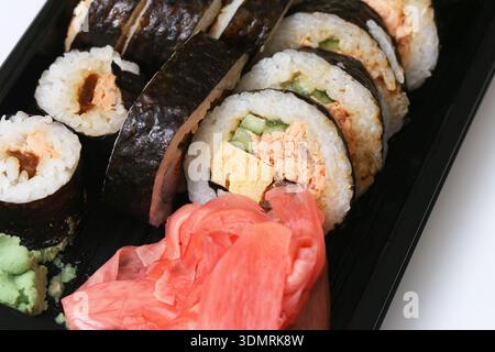 Sushi-Brötchen Nahaufnahme im Take-away-Container. Japanische Küche und asiatisches Speisekonzept mit Ingwer und frischen Zutaten. Stockfoto