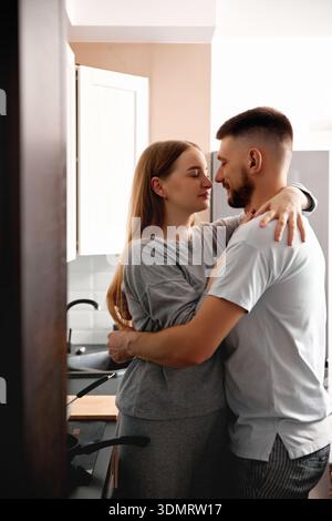 Ein Paar steht dicht in der Küche. Sie teilen einen zarten Moment beim gemeinsamen Kochen und genießen ihre Zeit im warmen Licht des Abends. Stockfoto
