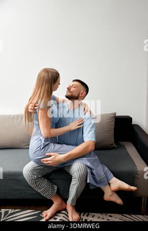 Ein Mann und eine Frau teilen sich einen Moment auf einer Couch in ihrem Wohnzimmer. Sie lächeln einander an, während die Frau auf dem Schoß sitzt. Ihr bequemer Clo Stockfoto