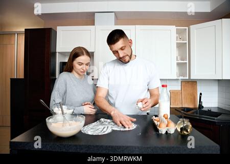Ein Mann und eine Frau sind in einer Küche. Sie mischen Teig und prüfen Zutaten, während sie ihre gemeinsame Zeit genießen, während sie eine Mahlzeit zubereiten. Stockfoto